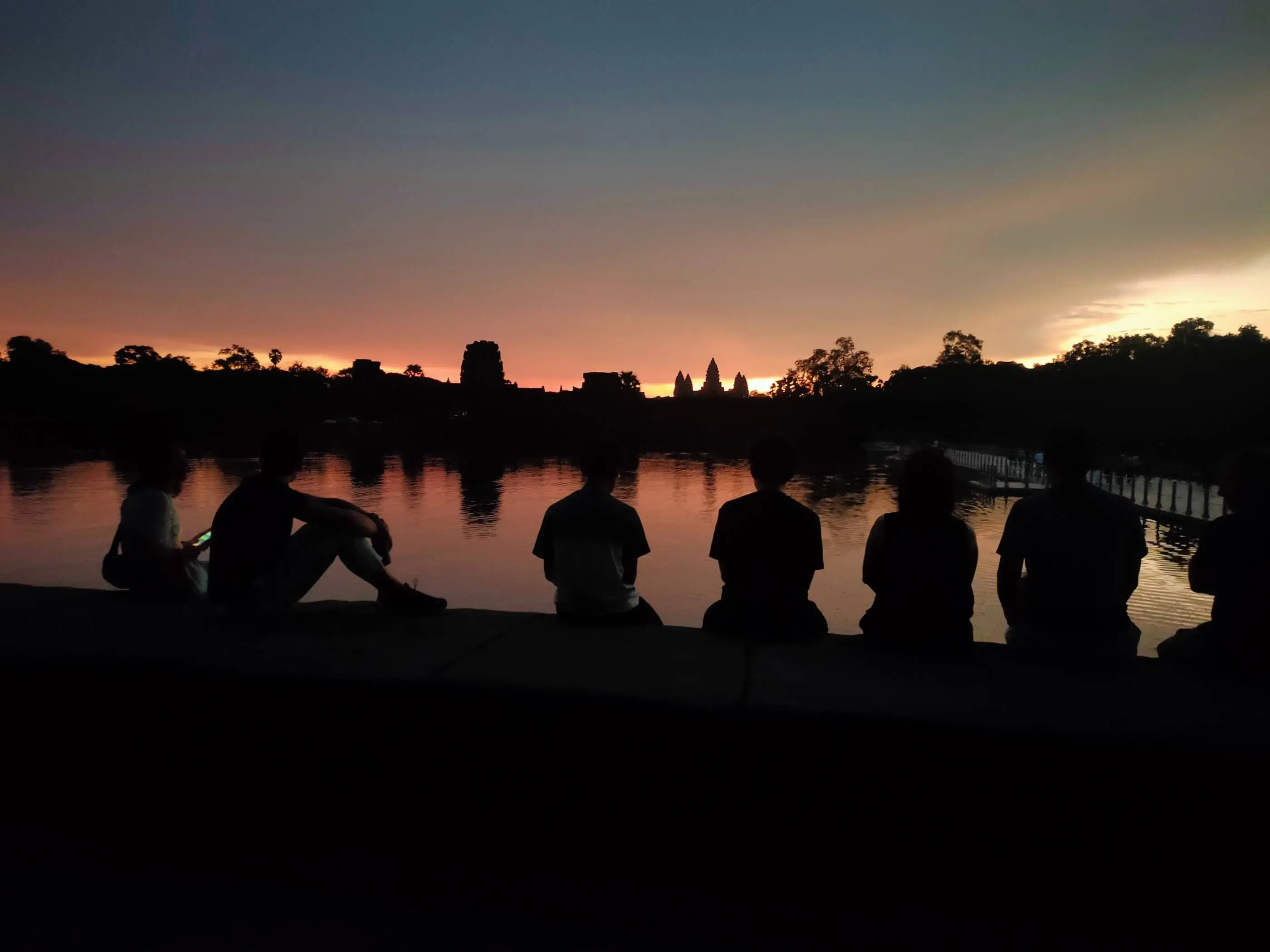 Amanecer en Angkor Wat, Siem Reap - Silueta del templo reflejada en el agua al alba, con los primeros rayos de sol iluminando las torres sagradas y cielo en tonos dorados.